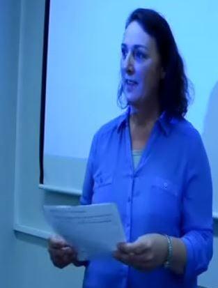 "A woman holding a document gives a presentation in a training setting."