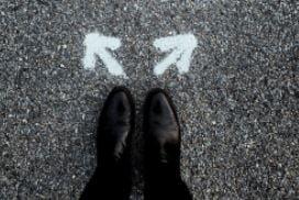 "Two shoes on a pathway stand in front of painted arrows pointing in opposite directions, symbolising choice or decision-making."