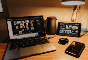 "An open laptop showing a virtual meeting with multiple participants, sur-rounded by various digital devices."