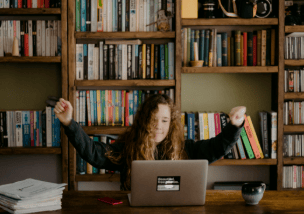 "A woman excitedly raising her arms while looking at a laptop screen, celebrating success or good news."