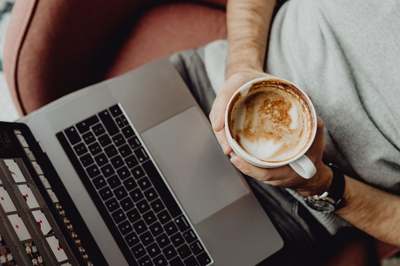 Man looks at his laptop computer holding a cup of coffee