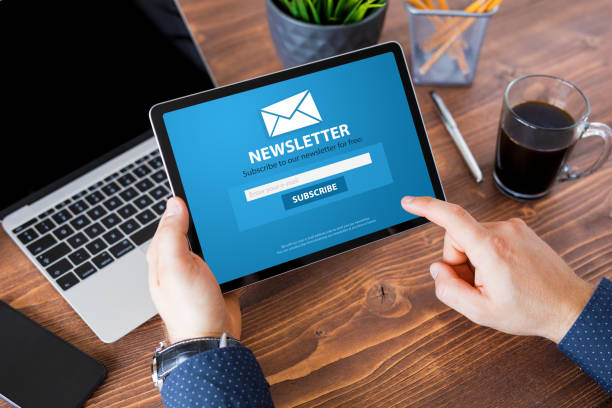 "A person uses their right hand to interact with an online newsletter displayed on an iPad held in their left hand."