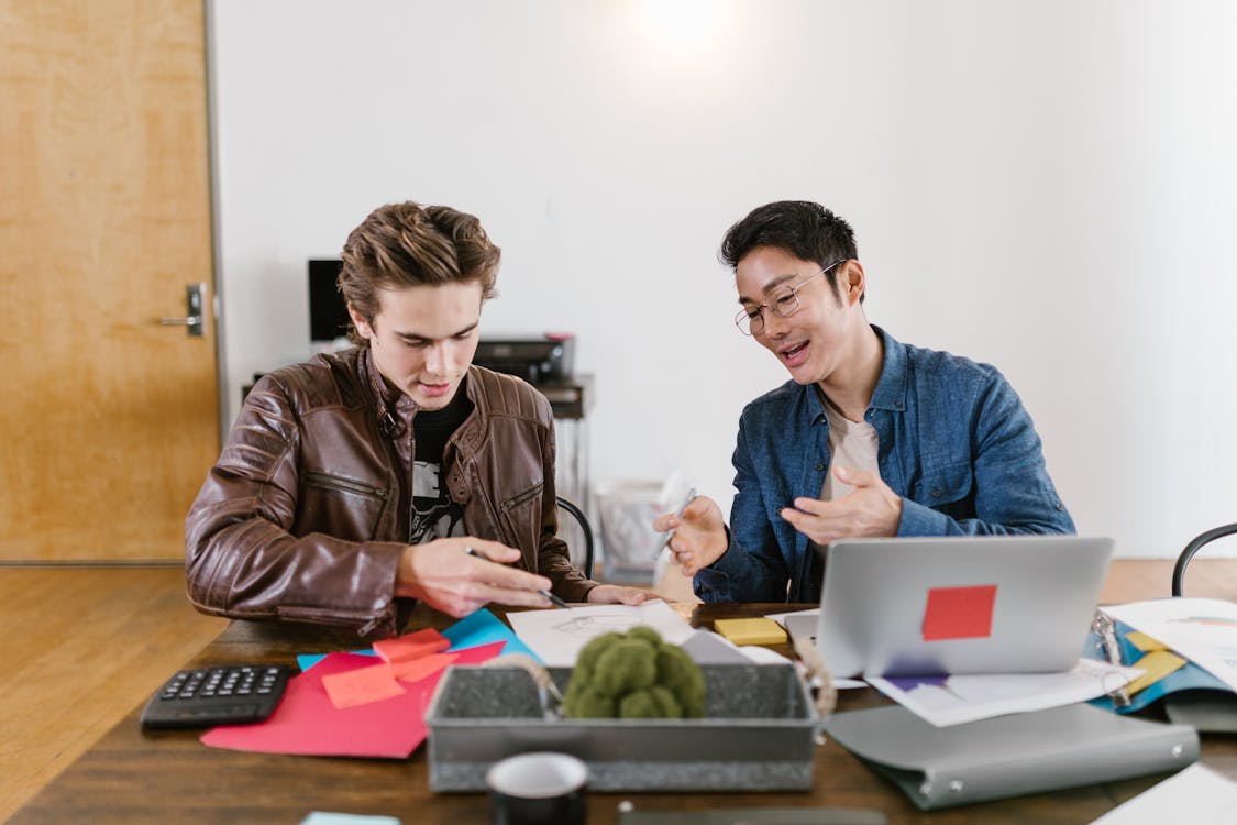 "A person seated with a support person in front of a laptop, receiving guidance to engage in an activity."