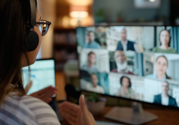 "A person seated at a desktop computer gesturing to a computer screen of multiple people in an online meeting."